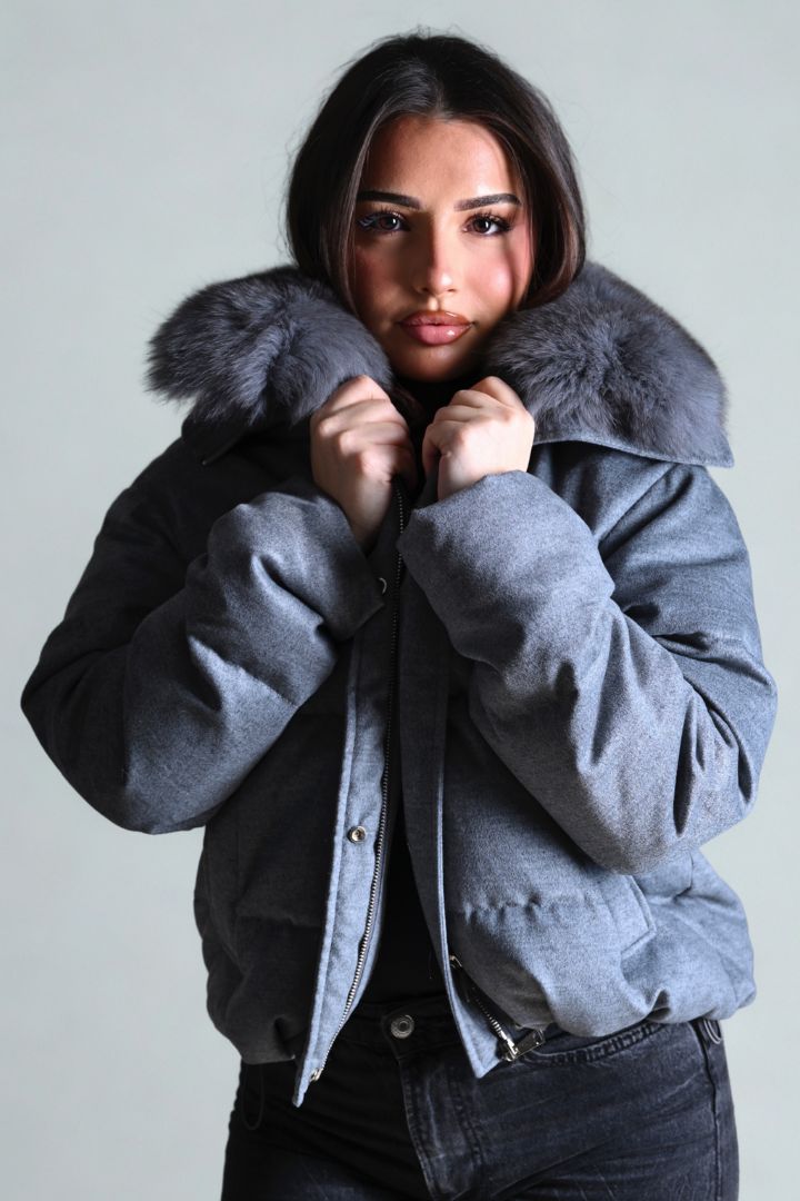 Woman wearing a gray coat with fur collar against a plain background