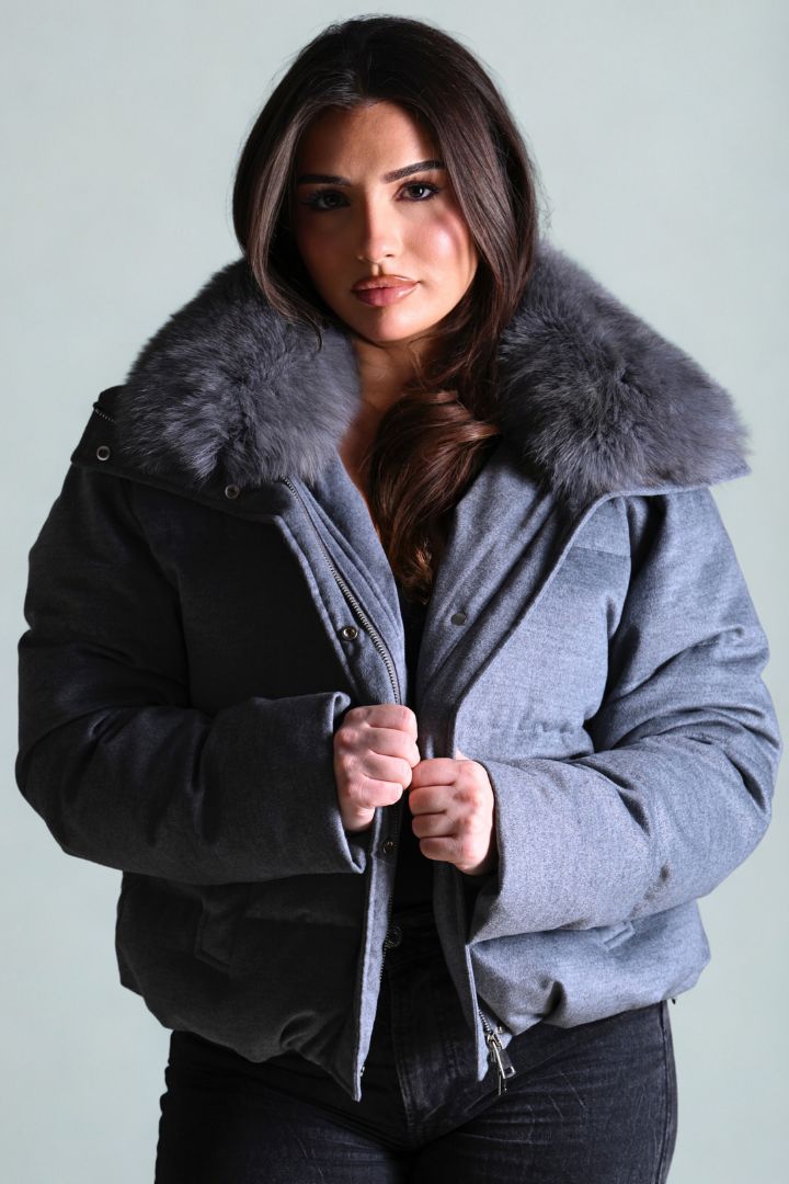 Woman wearing a gray coat with a fur collar against a light background