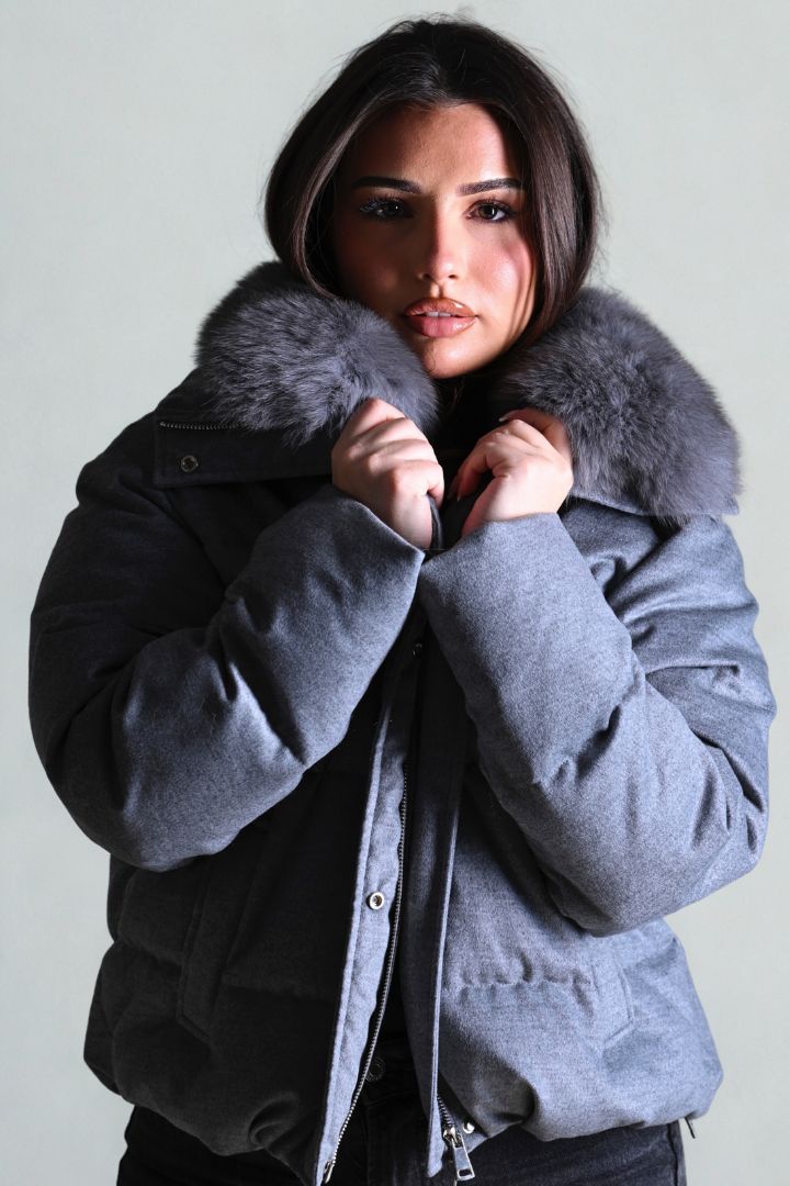 Woman wearing a gray winter coat with a fur-lined hood against a plain background