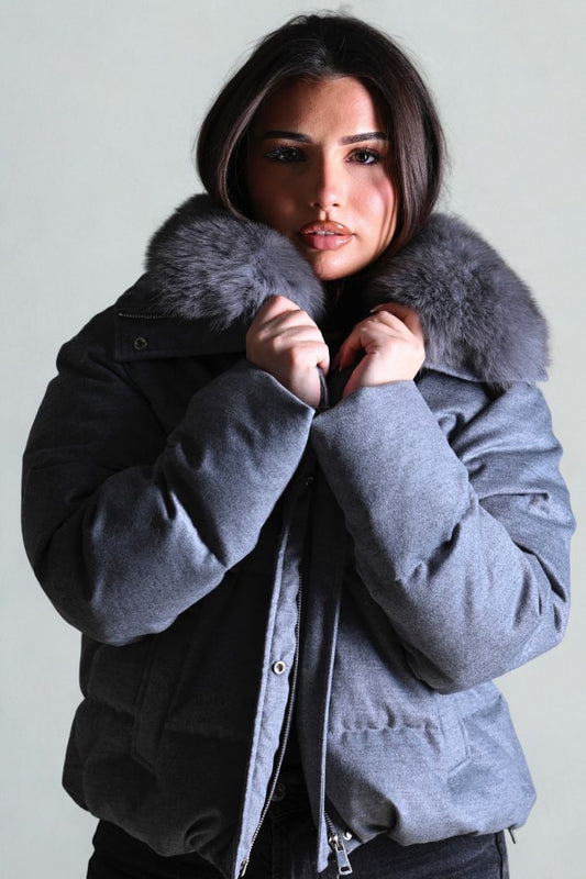 Woman wearing a gray winter coat with a fur-lined hood against a plain background
