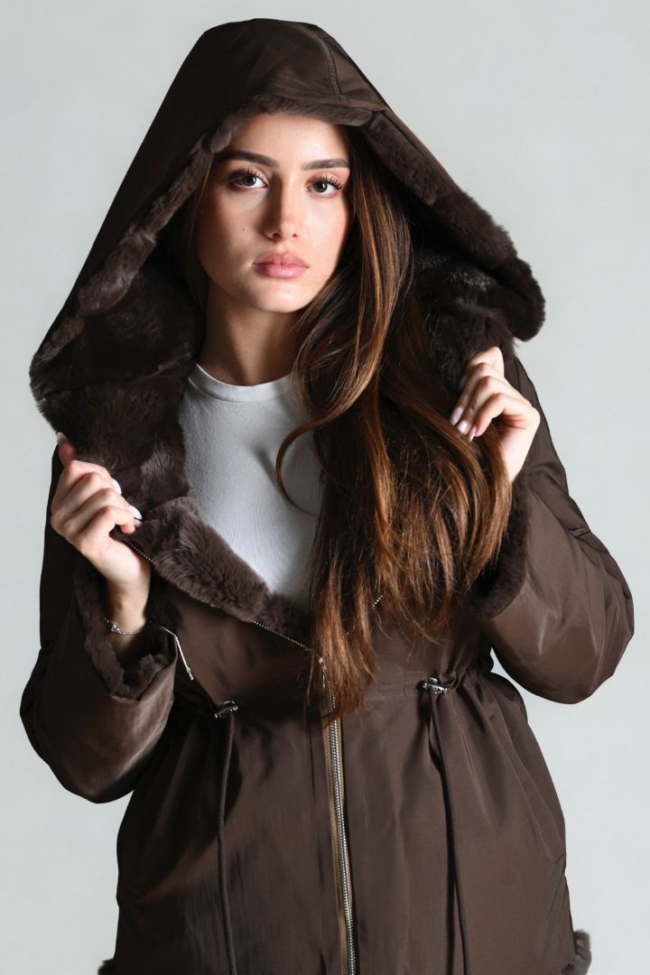 Woman wearing a brown hooded coat against a plain background