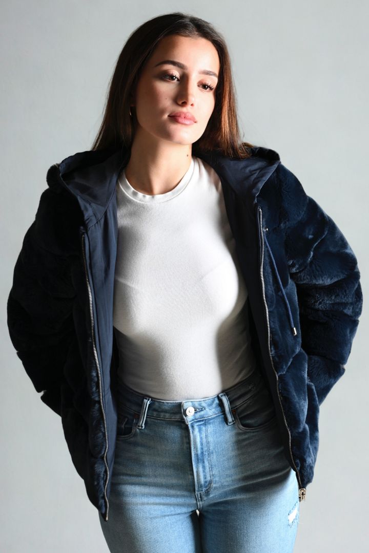 Woman wearing a navy blue jacket over a white shirt and blue jeans on a gray background