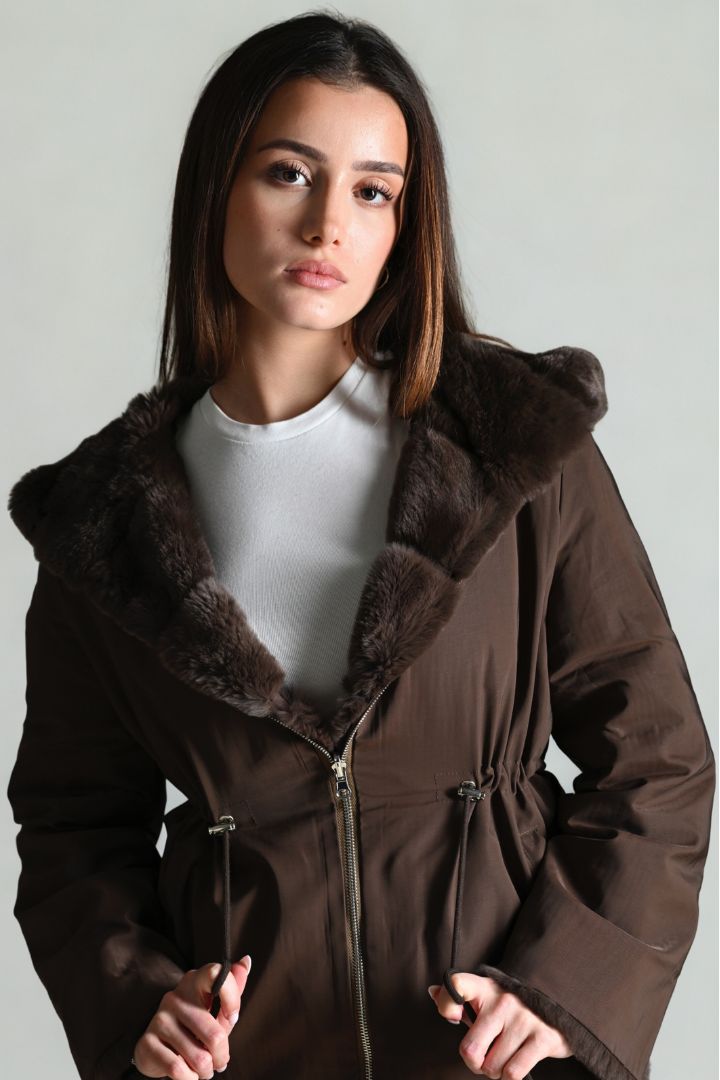 Woman wearing a brown coat with fur trim against a plain background