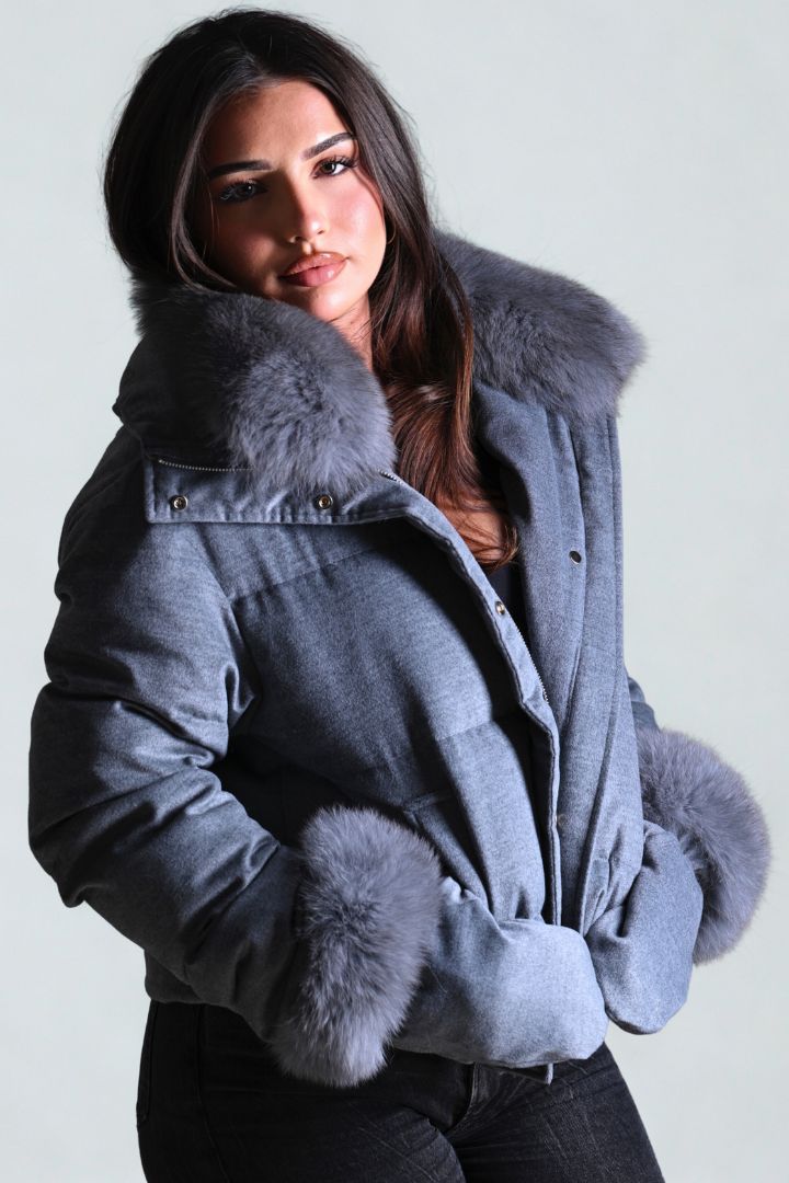 Woman wearing a blue coat with fur trim against a plain background