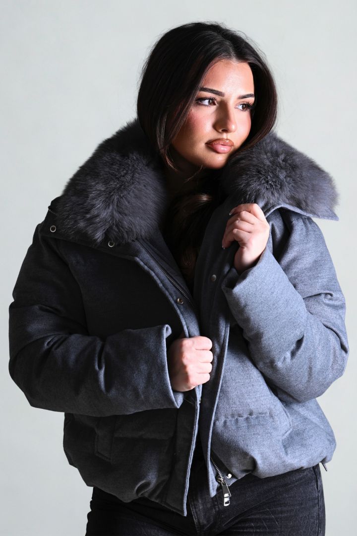 Woman wearing a gray coat with a fur collar against a plain background