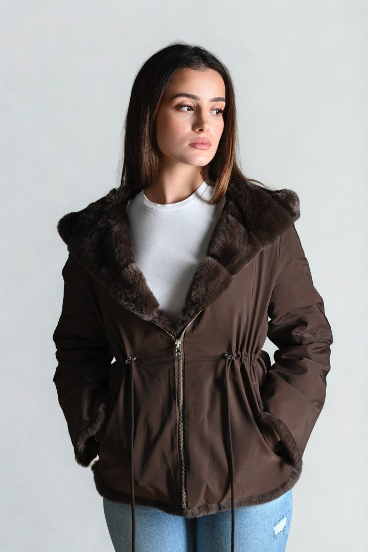 Woman wearing a brown coat with fur trim against a plain background