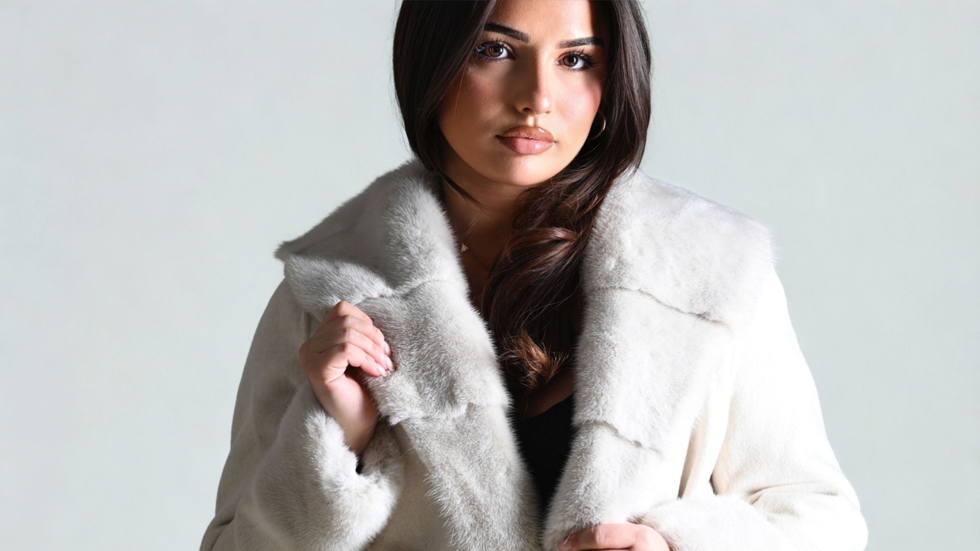 Close-up of a woman modeling a white fur coat, highlighting the soft collar and luxurious texture.