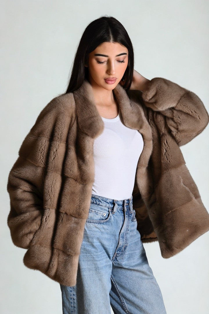 Woman wearing a brown fur coat over a white top and blue jeans on a plain background